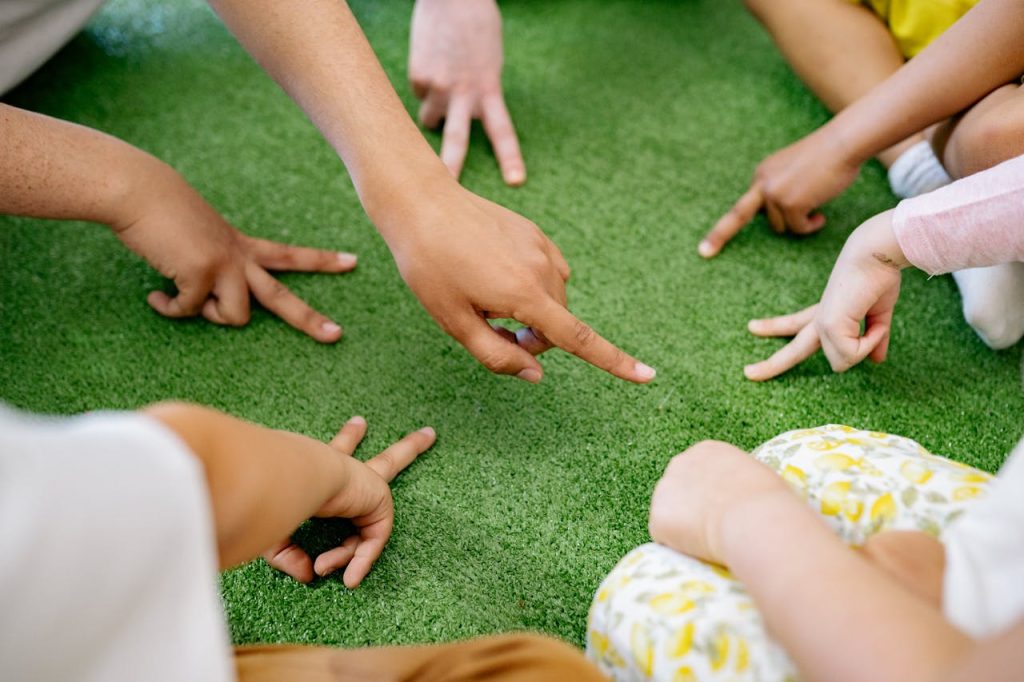 Group of diverse children playing a finger game on green grass, promoting fun and friendship.
