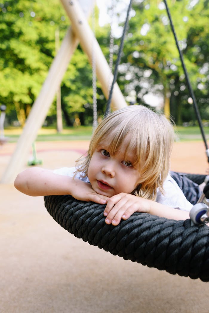 Adorable blond child resting on a swing at a sunny playground.