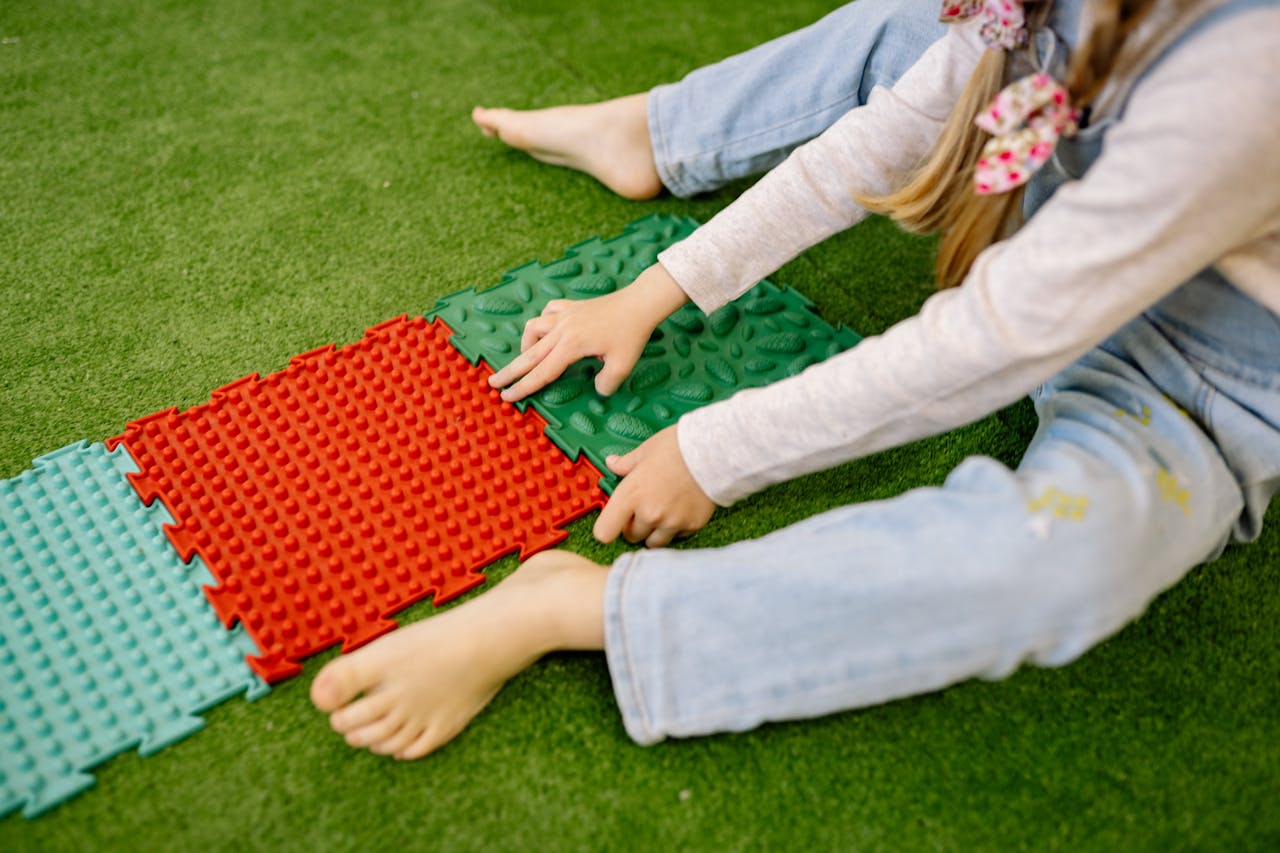 A child plays with colorful textured mats on grass, enjoying outdoor recreation.