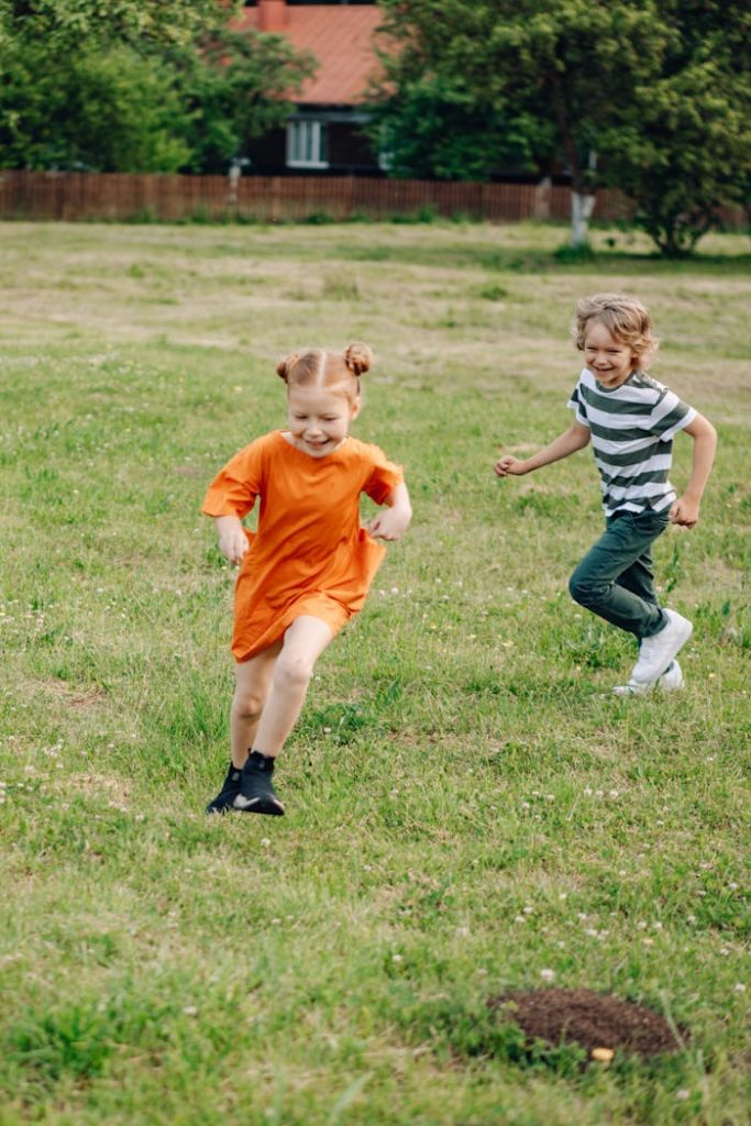 Two children playfully running on a sunny day in a lush green park.